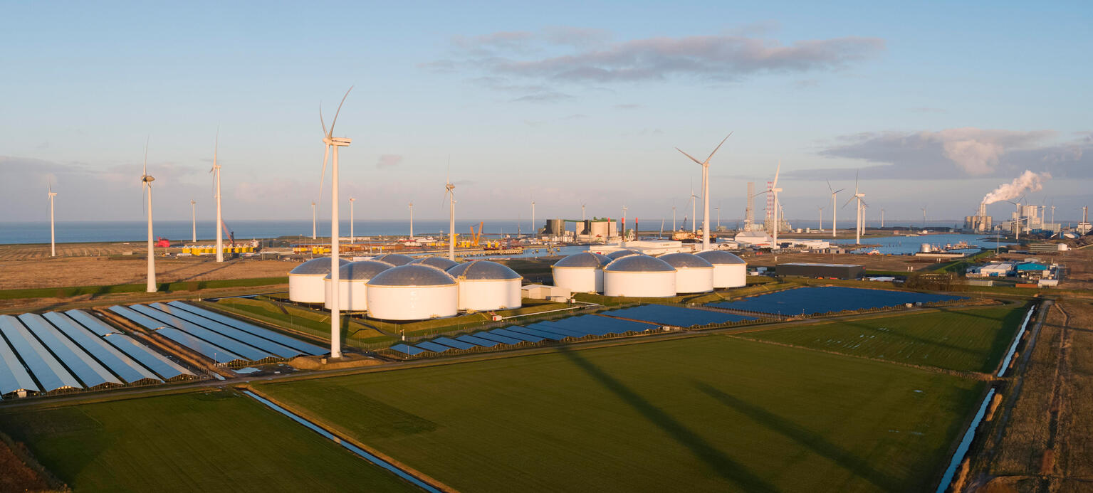 Wind turbines near solar panels with crude oil storage and coal fired power stations