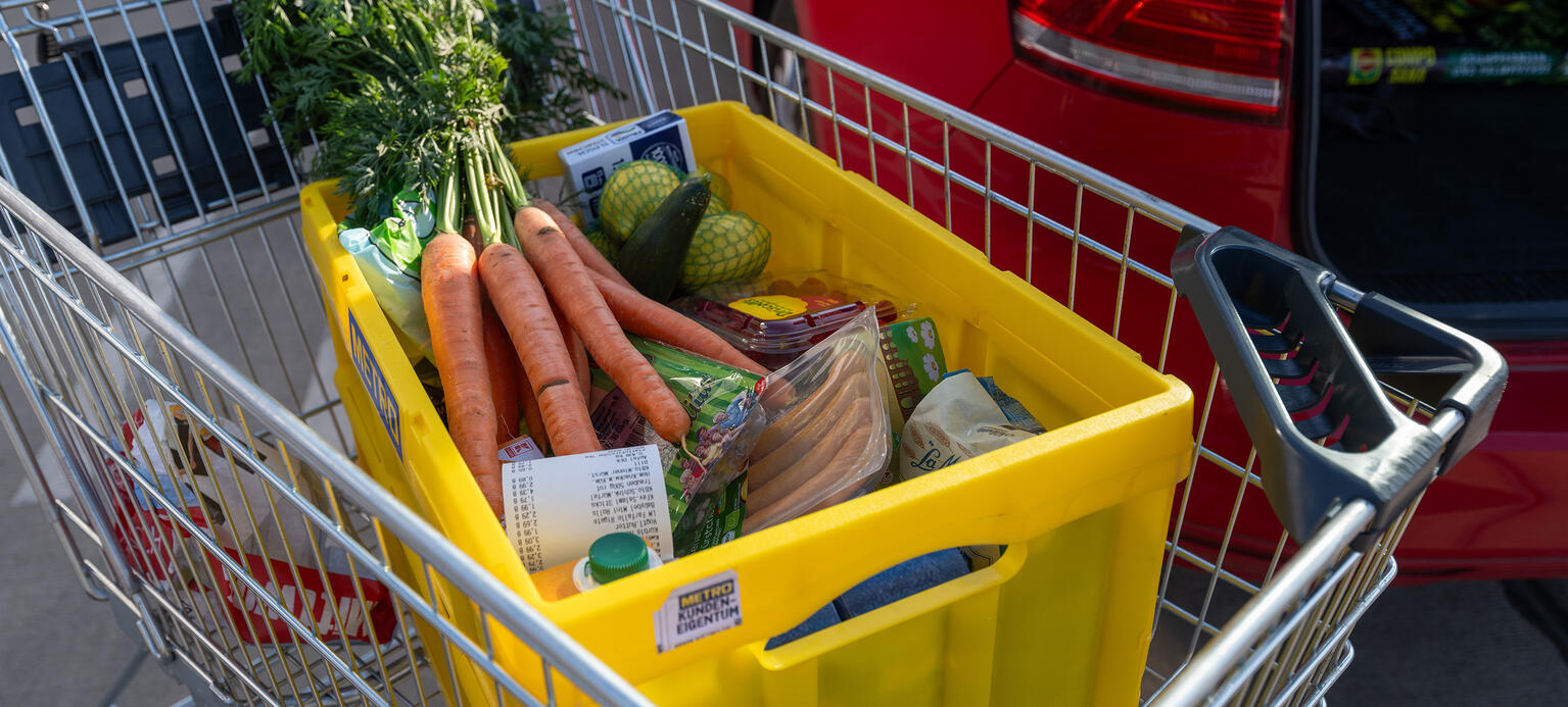 Eine Einkaufskiste mit Lebensmitteln steht in einem Wagen auf einem Parkplatz eines Supermarktes.