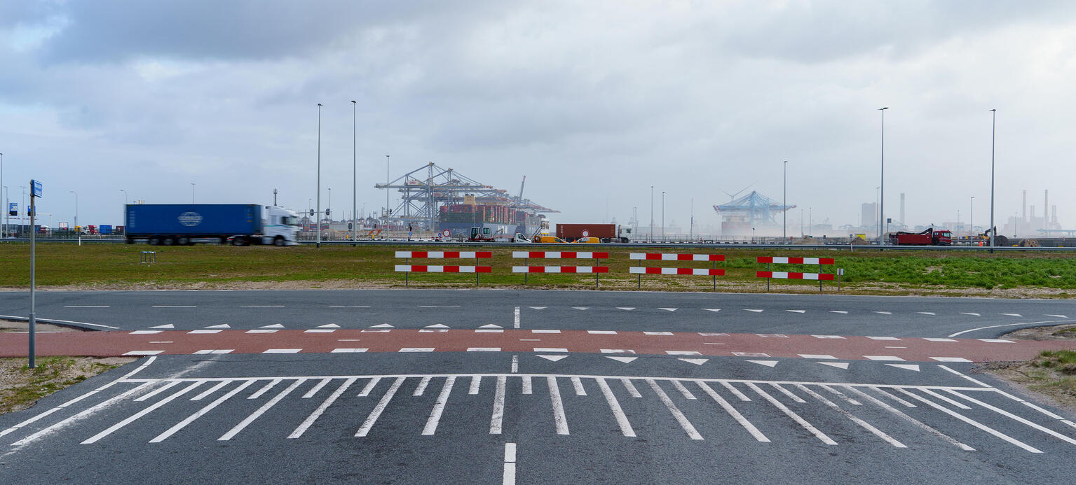 Containerschiffe liegen im Hafen. Im Vordergrund ist eine Straßenkreuzung zu sehen.