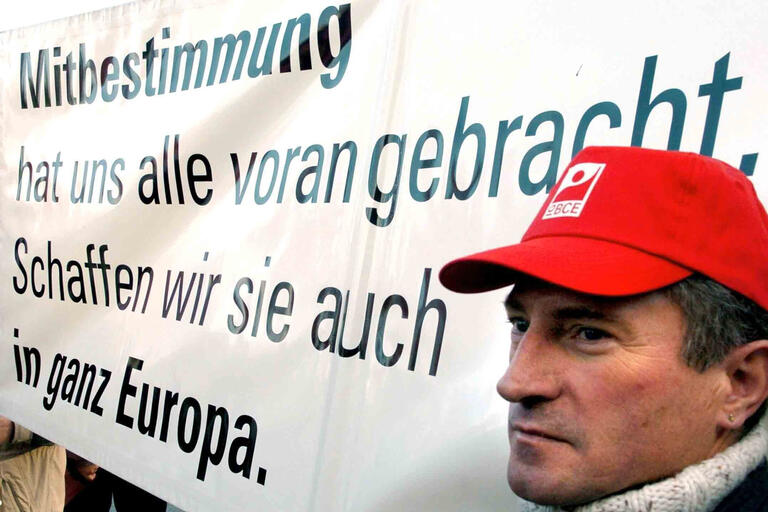 Ein Gewerkschaftsmitglied steht neben einem Plakat mit der Aufschrift 'Mitbestimmung hat uns alle voran gebracht. Schaffen wir sie auch in ganz Europa.' 